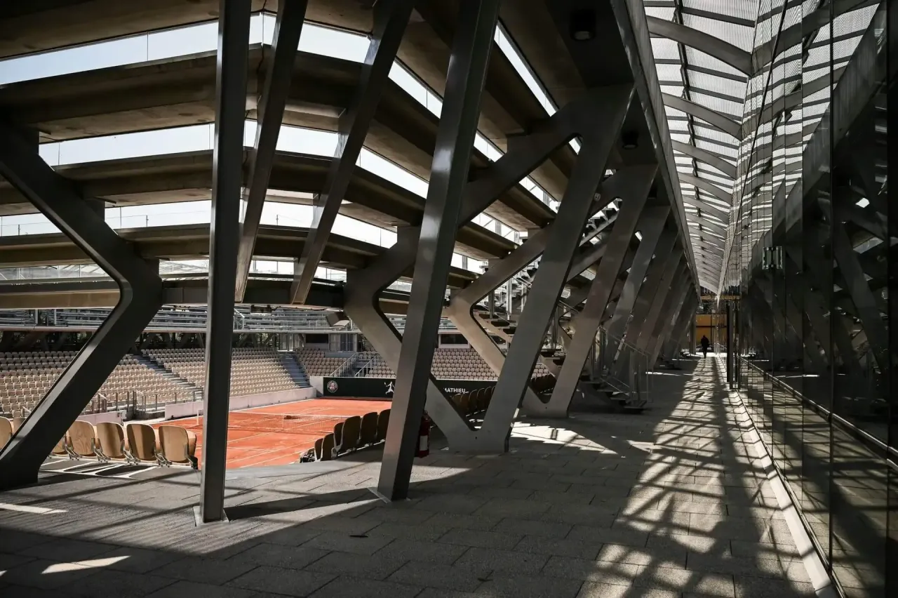 A clay tennis court peeks out from behind greenhouses at the French Open.